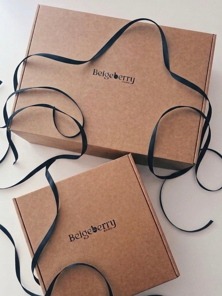 Two brown kraft paper gift boxes with the brand name 'Belgeberry' printed on them, tied with long black ribbons on a light background.