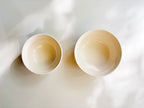 Two small white ceramic cups viewed from above on a white surface with soft natural shadows.