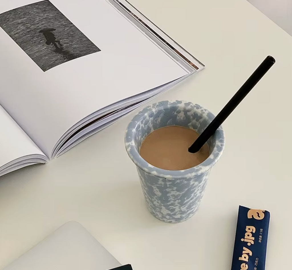 Cup of coffee with a straw on a table next to an open book and a blue packet.