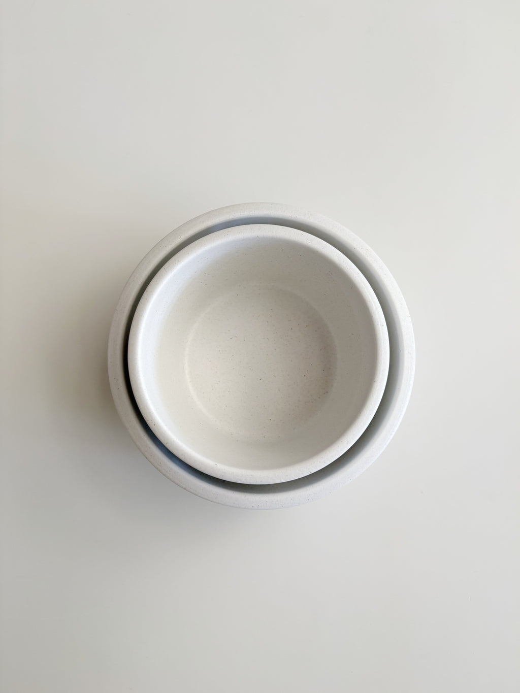 Three nested white ceramic bowls stacked vertically, viewed from directly above on a light gray background.