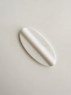 A glossy white, elongated oval-shaped spoon rest, possibly a decorative soap dish or a small sculptural vessel, shown on a plain light beige background.