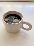 White ceramic mug with a handle filled with dark liquid on a white surface